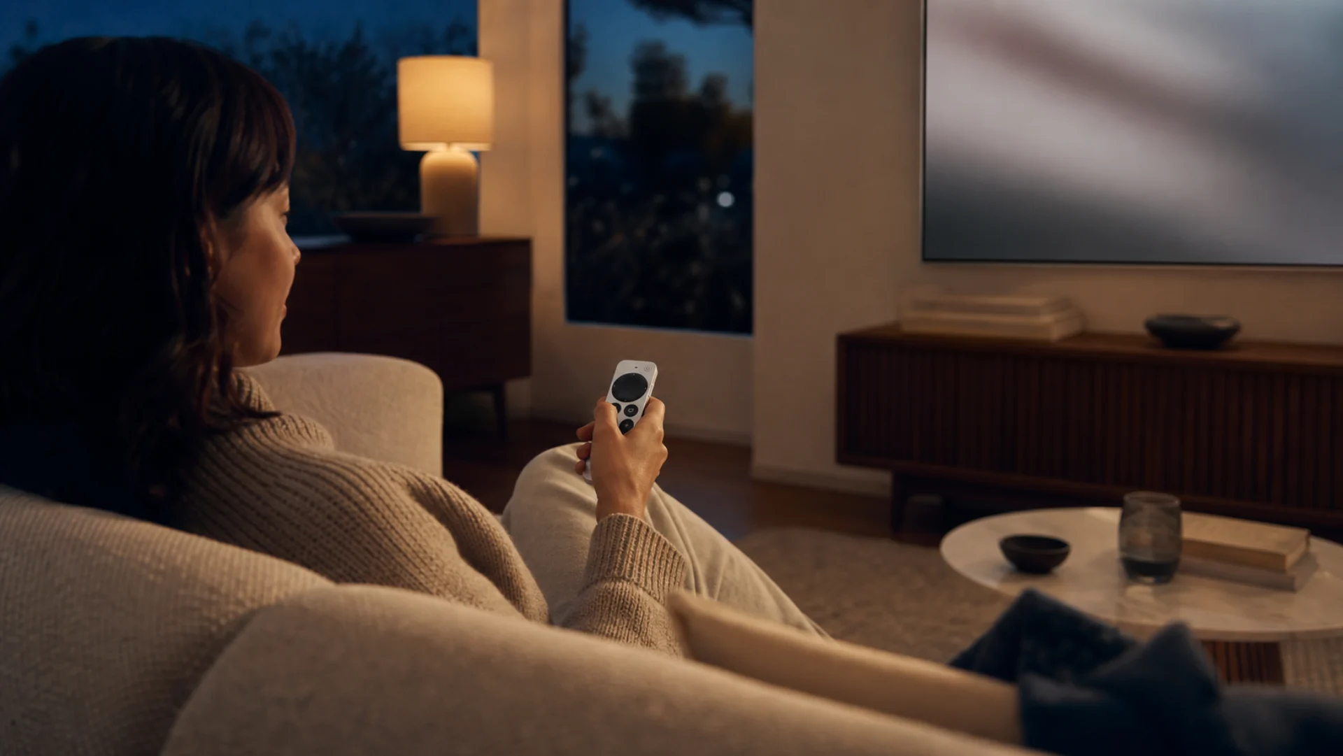 Person controlling a Mac with a Siri Remote from a comfortable sofa